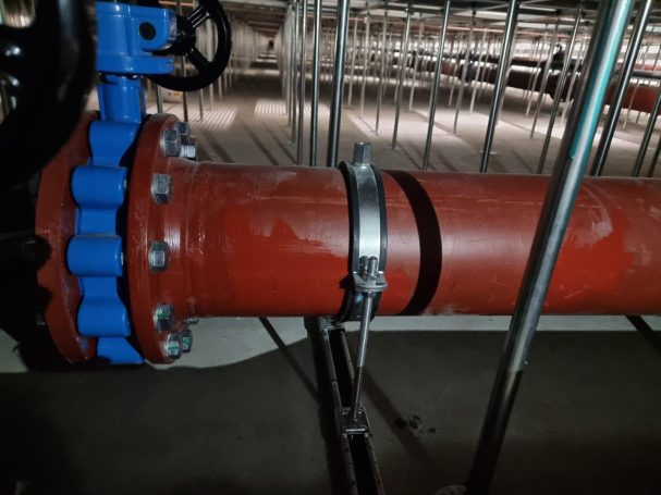 Rode pijp met een blauwe klep en metalen klemmen in een industriële omgeving.